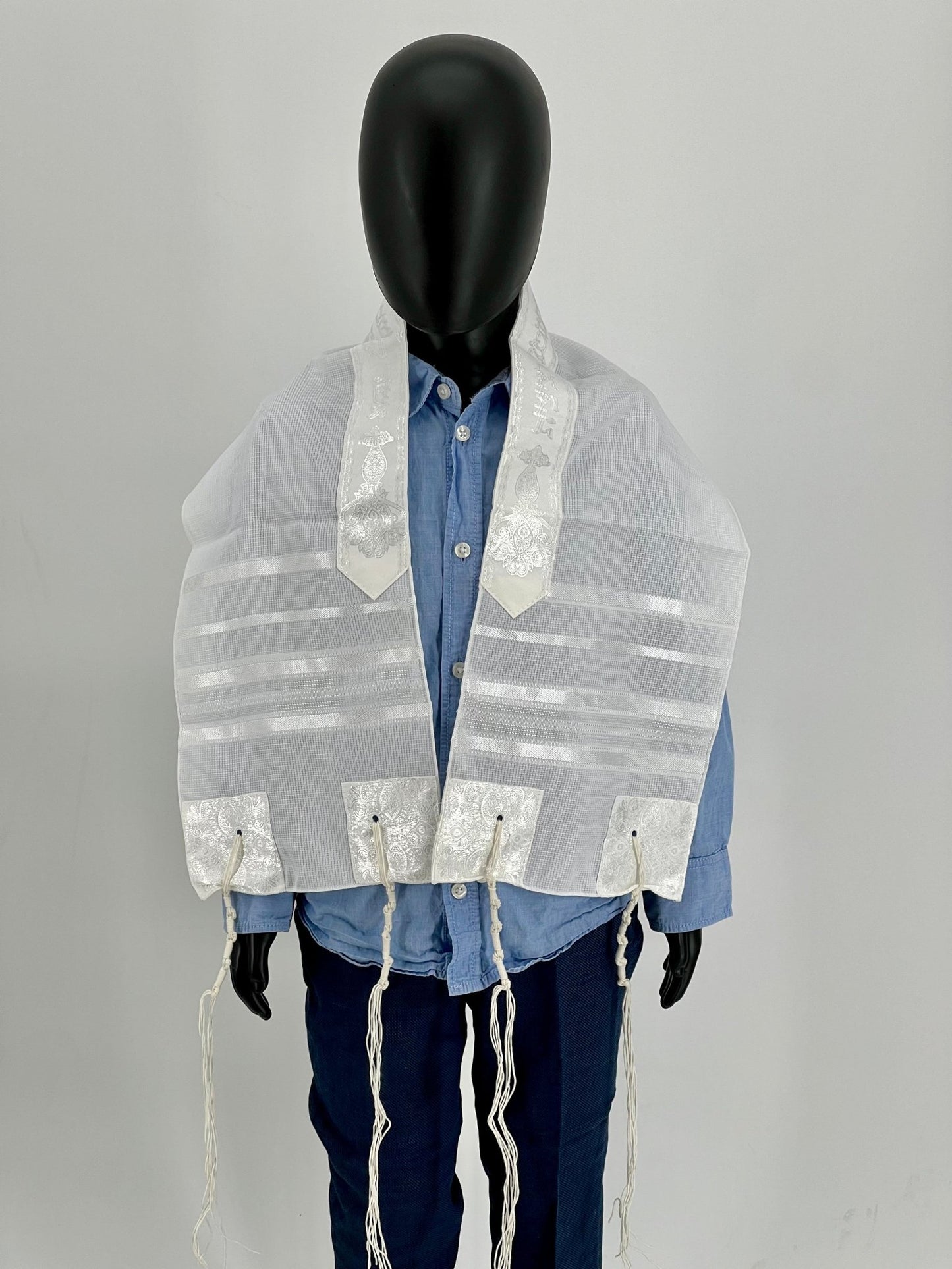 Child mannequin wearing a white children's tallit (Jewish prayer shawl) with white stripes and white embroidered corners