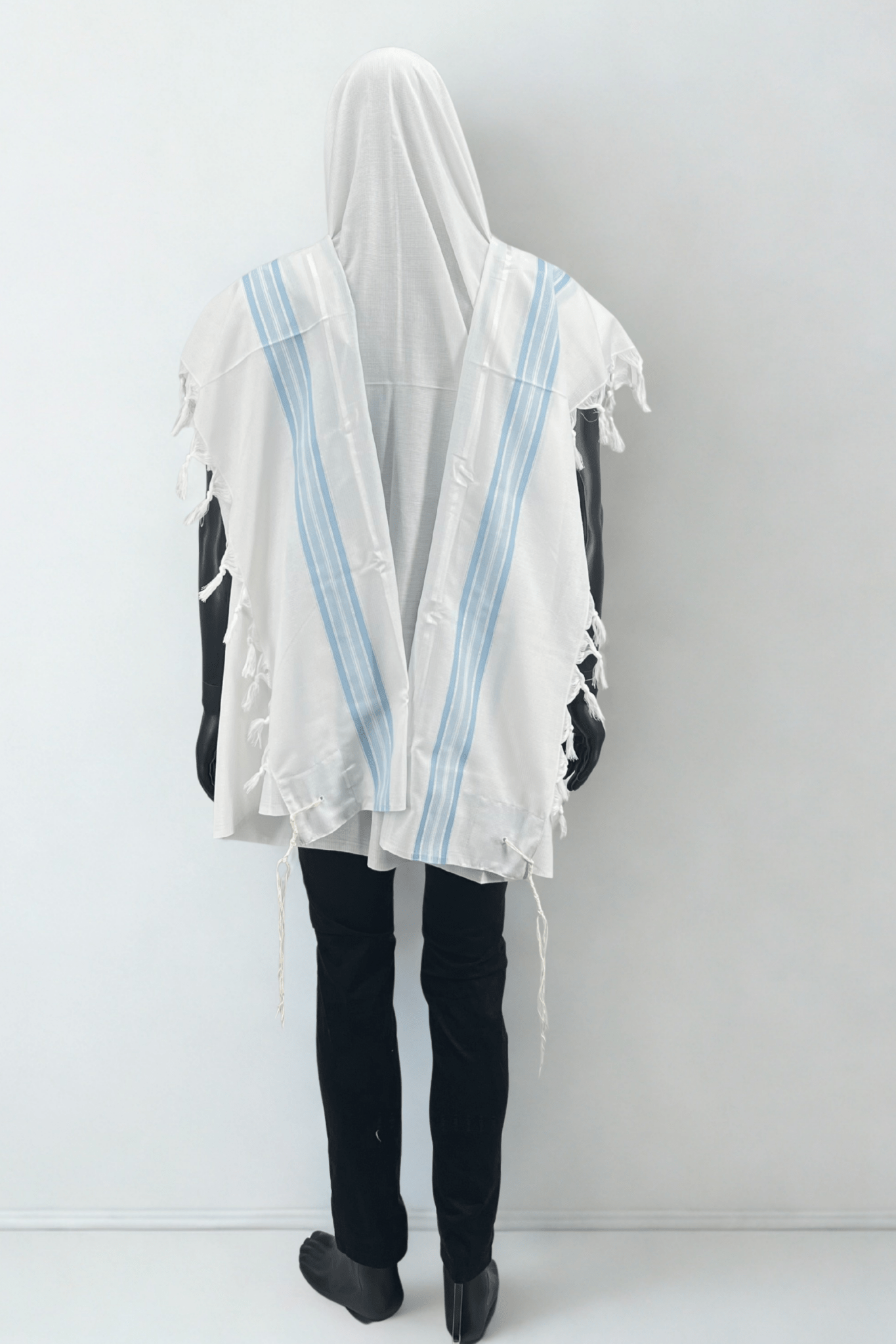 Mannequin wearing a white prayer shawl with blue stripes on a plain background