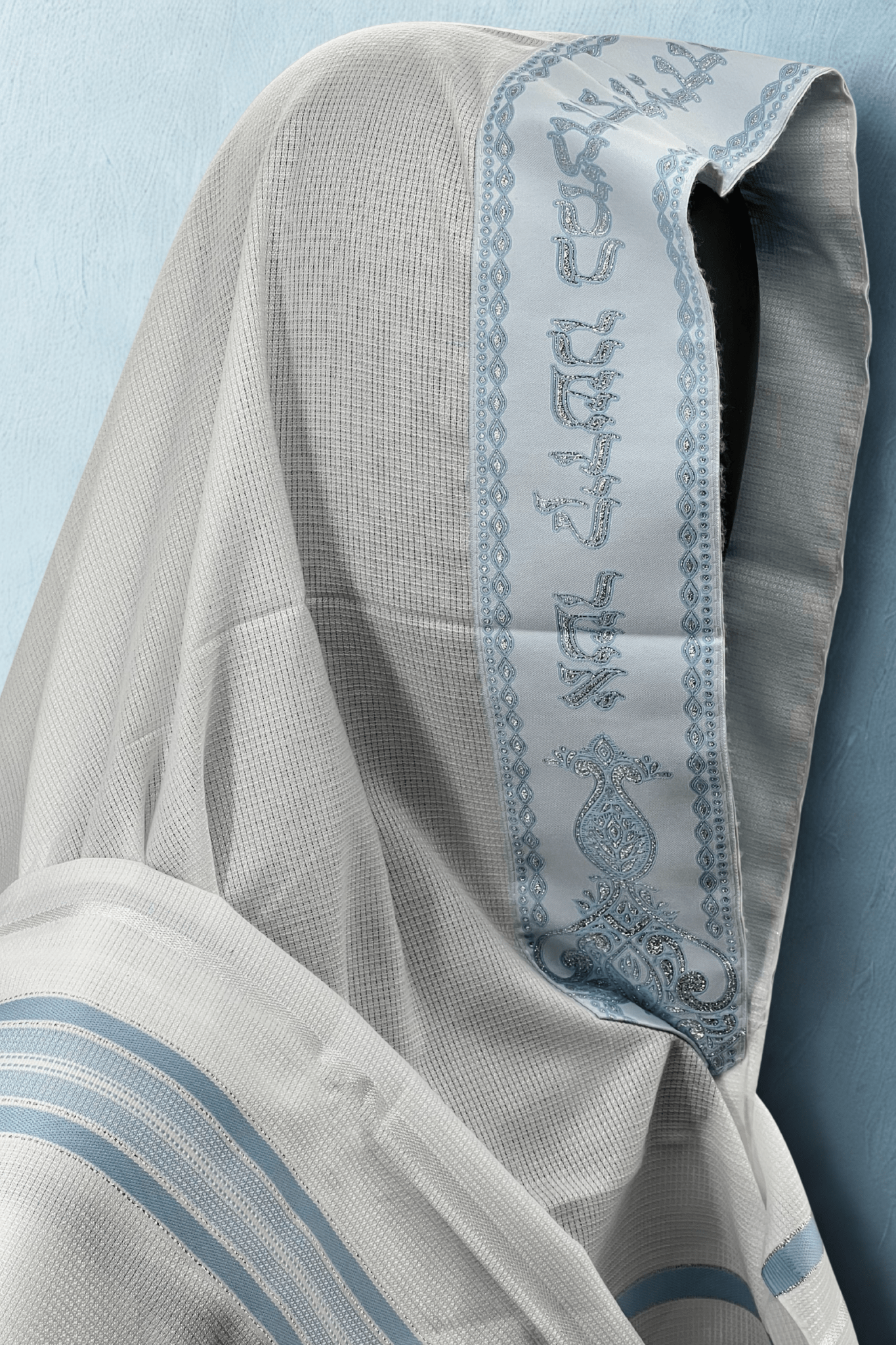 Close-up of a Tallit Chatanim with blue embroidery on a light blue background