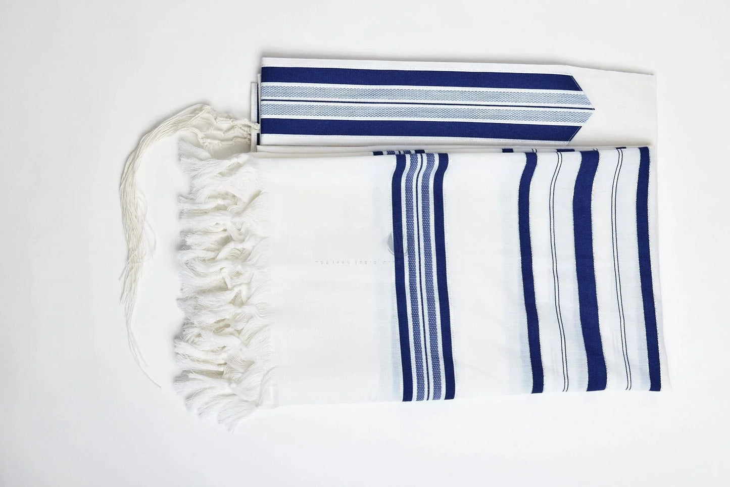 A white tallit with blue and white stripes, featuring a fringed edge and a tassel at the corner.