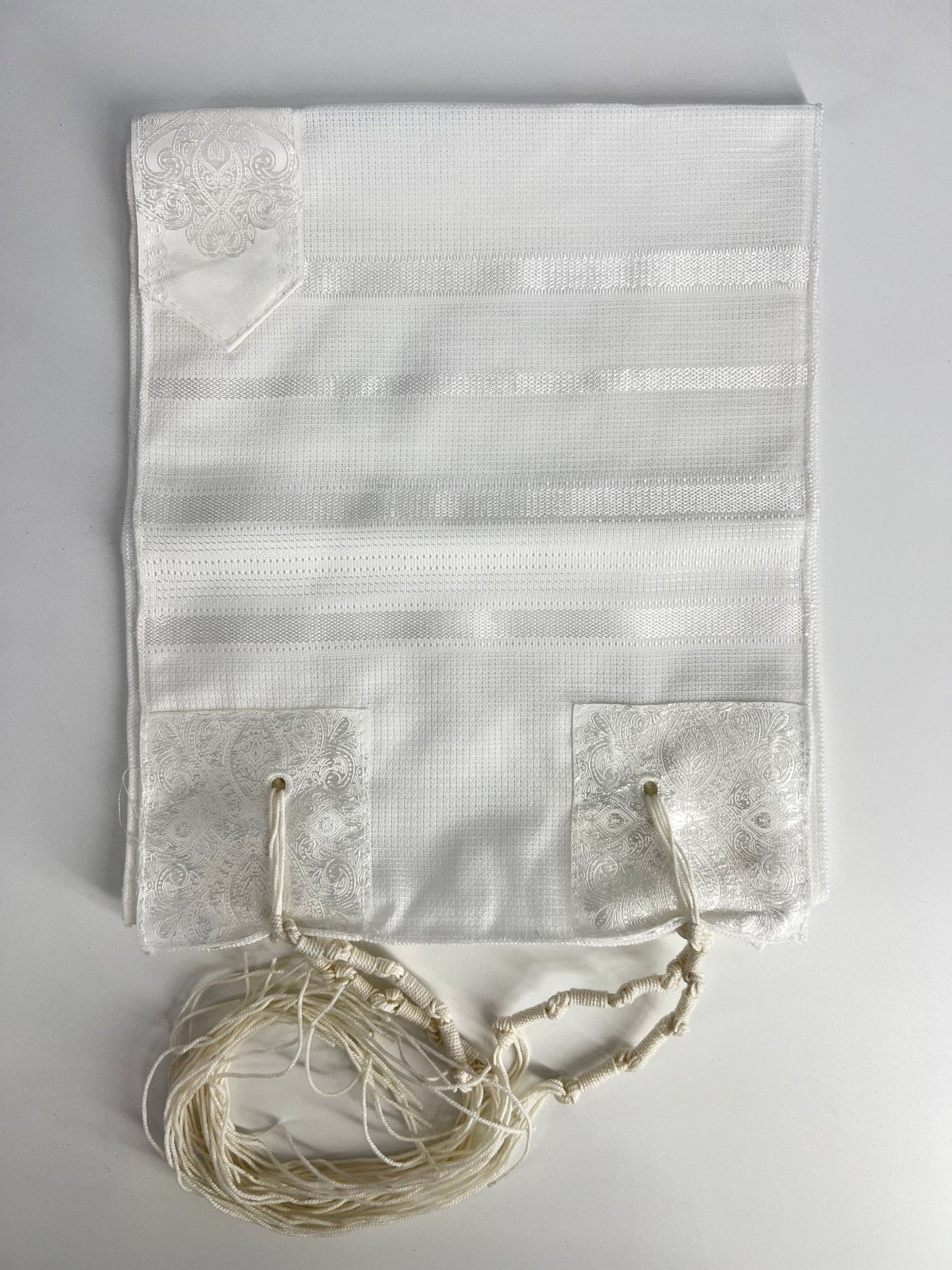 Folded white children's tallit (Jewish prayer shawl) featuring silver stripes, decorative silver corner reinforcements
