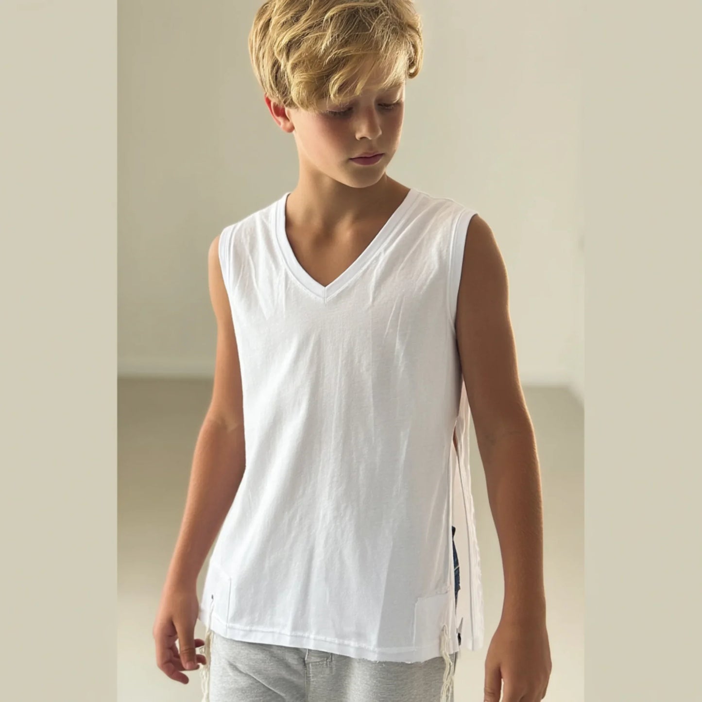 Young boy wearing a white Tzitzit T-shirt sleeveless and gray pants against a plain background