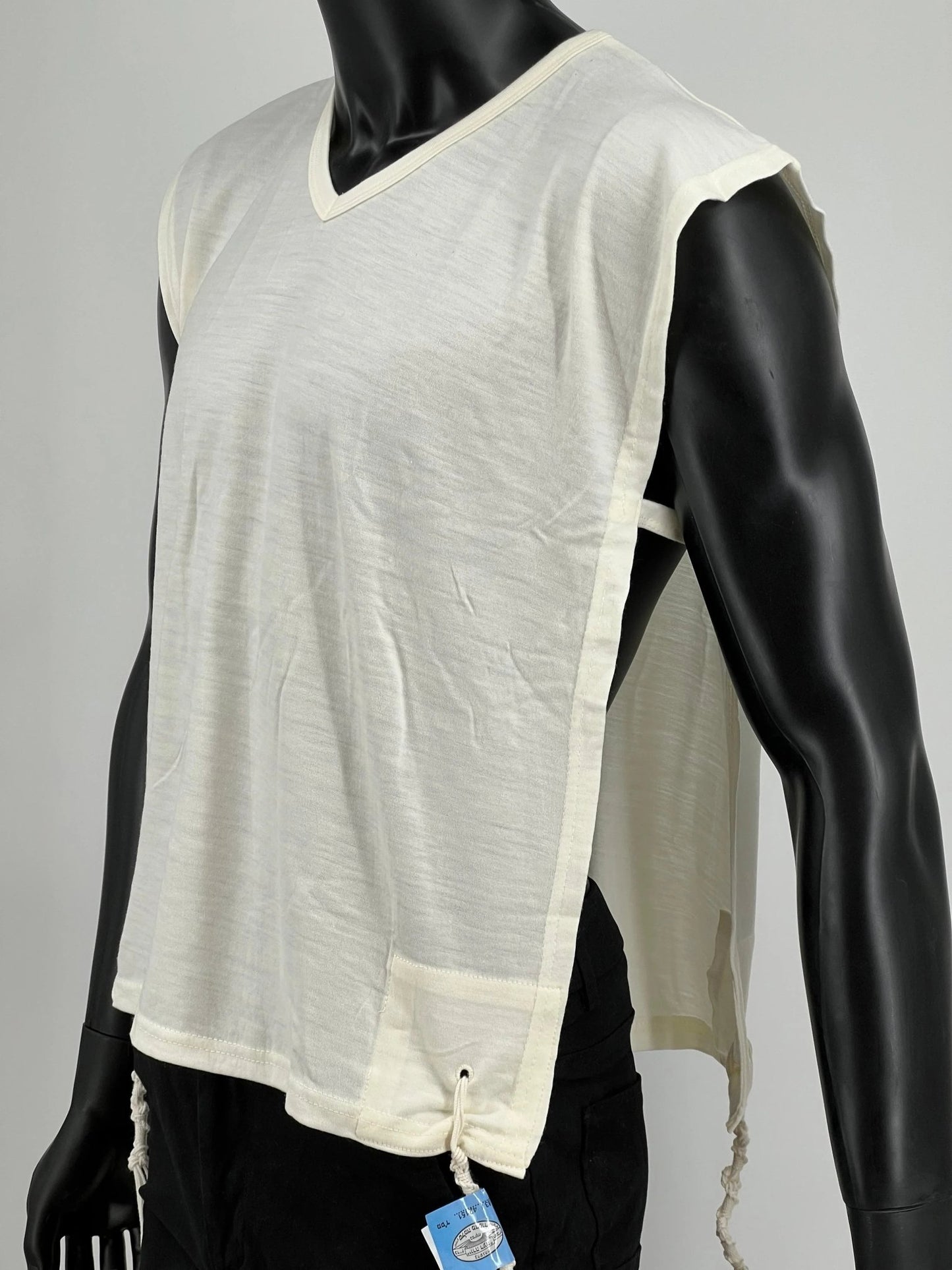 White wool Tzitzit T-shirt vest displayed on a mannequin torso. Made from 100% lamb’s wool, the garment features a wide halachic V-neck opening