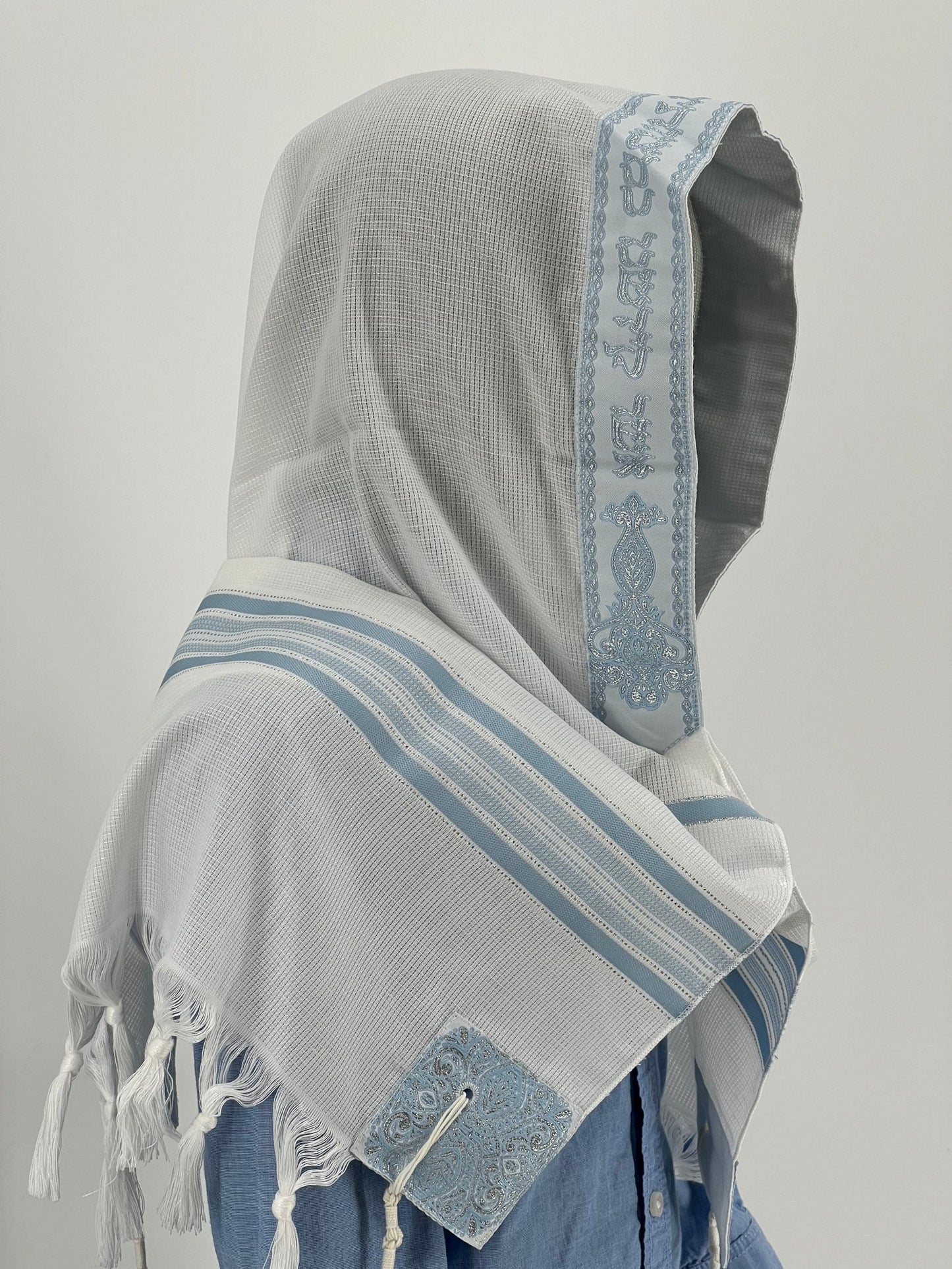 Child mannequin wearing a white tallit prayer shawl with light blue stripes and a silver atarah