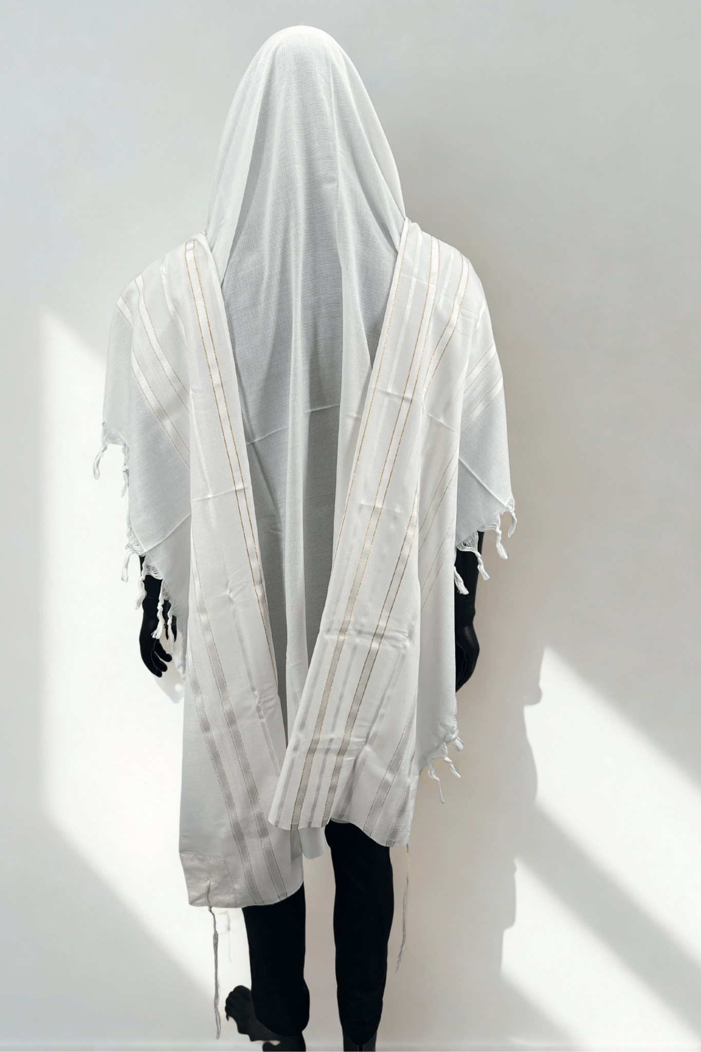 mannequin wearing a white Acrylic Tallit Chatanim with gold stripes, draped with a hood. The tallit features kosher tzitzit