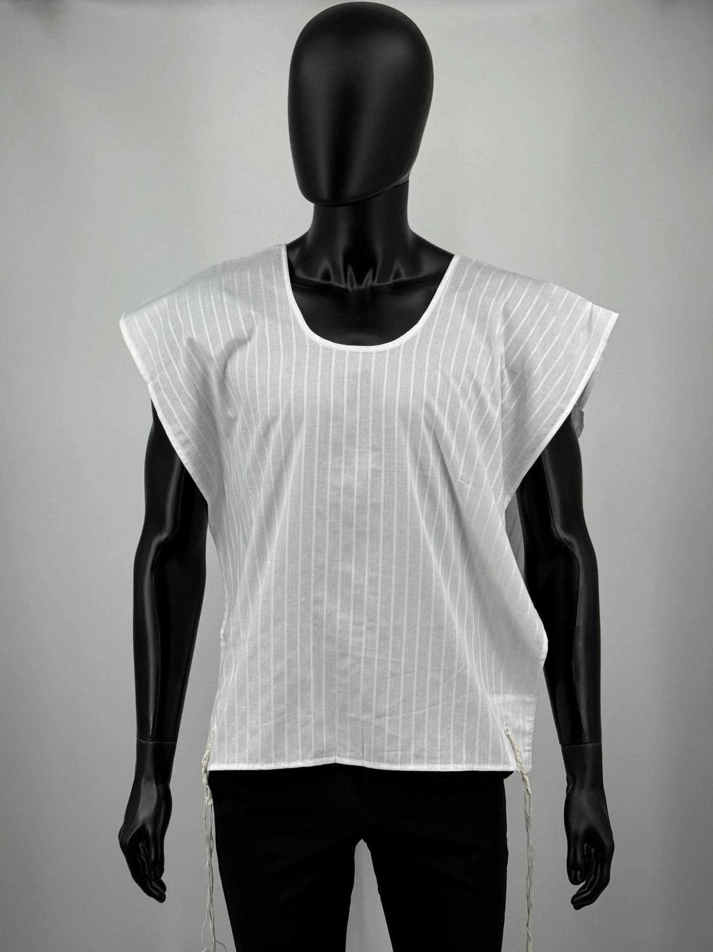 A white cotton Tallit Katan with vertical textured stripes, shown on a black mannequin torso. The garment features a V-shaped neckline and tzitzit strings hanging from the two front corners.