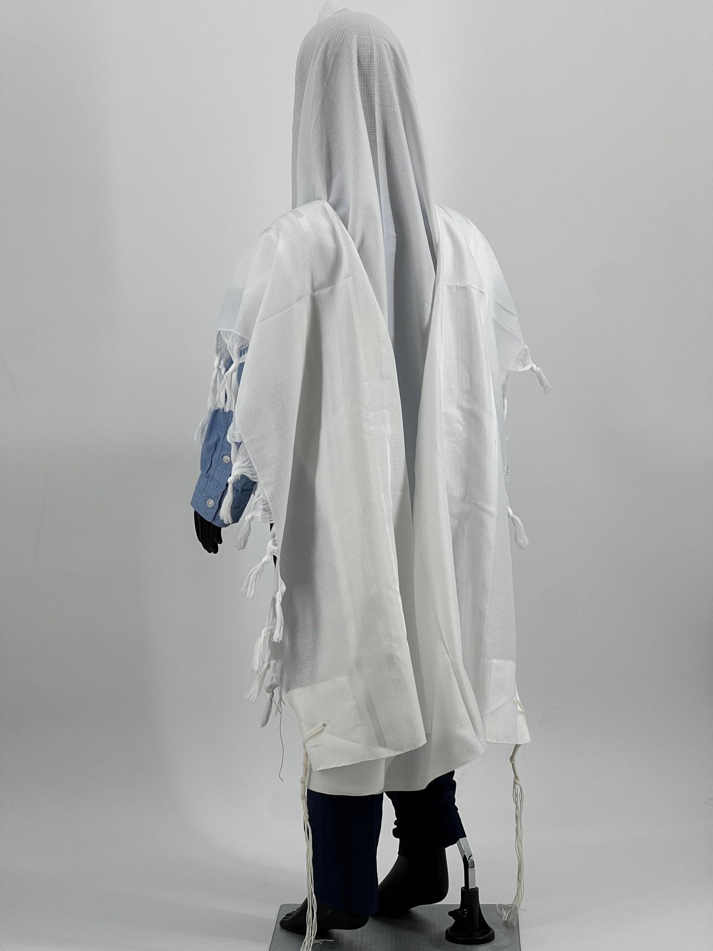 Child mannequin dressed in a white tallit (Jewish prayer shawl) viewed from a rear side angle.