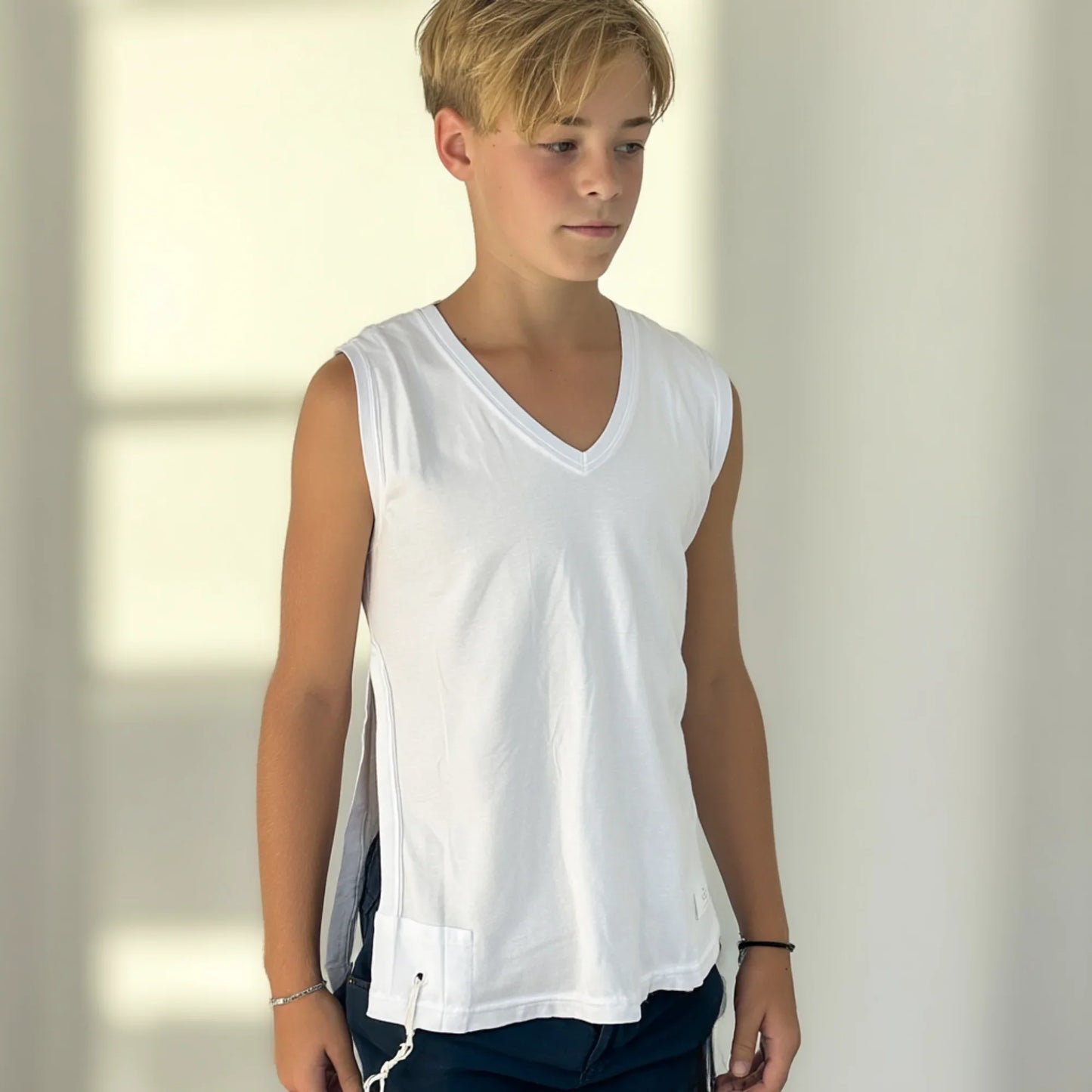 Boy wearing a white sleeveless Tzitzit T-shirt against a neutral background