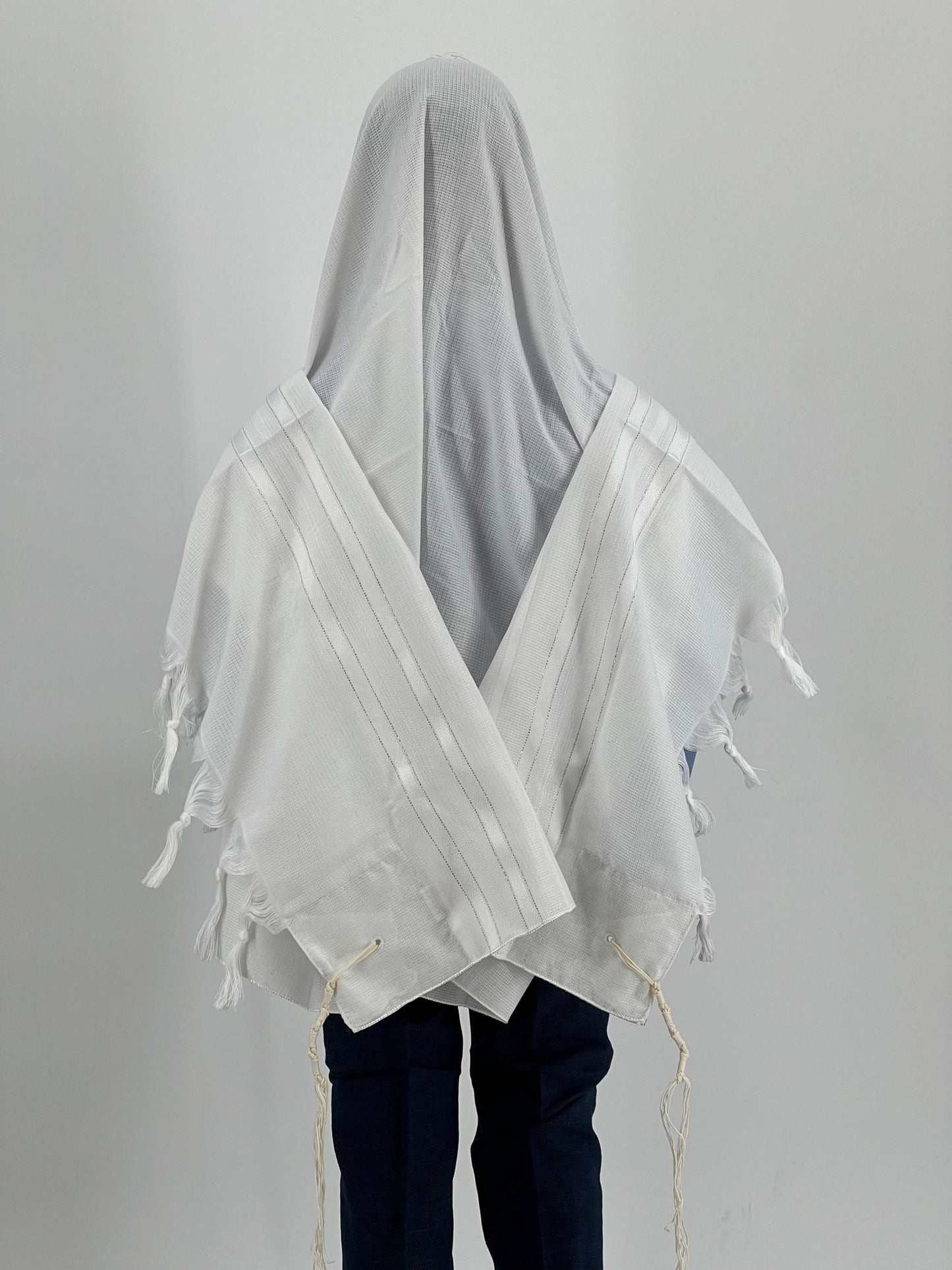 Child wearing a white tallit (Jewish prayer shawl) with subtle white-on-white striping, viewed from the back.