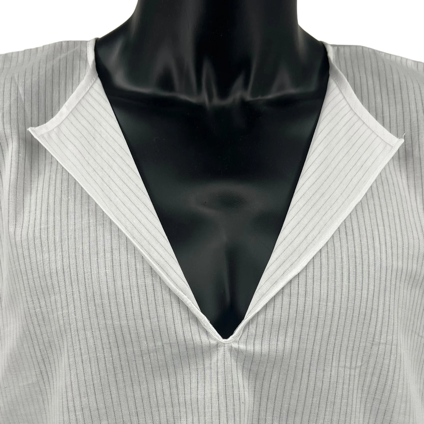 Close-up front view of a white cotton Tallit Katan worn on a black mannequin torso. The garment features a V-neck opening, fine vertical stripes