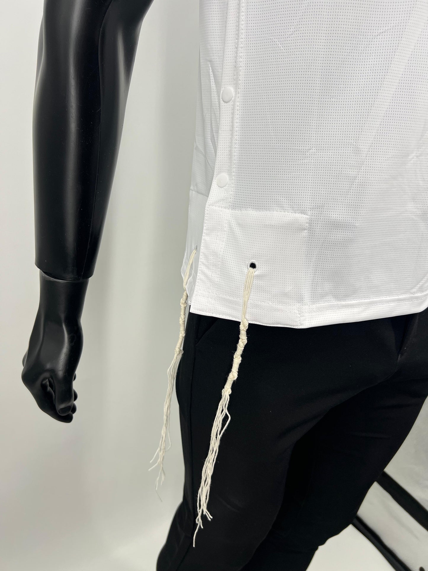 Mannequin wearing a white tzitzit tank top with fringes and black pants against a plain background