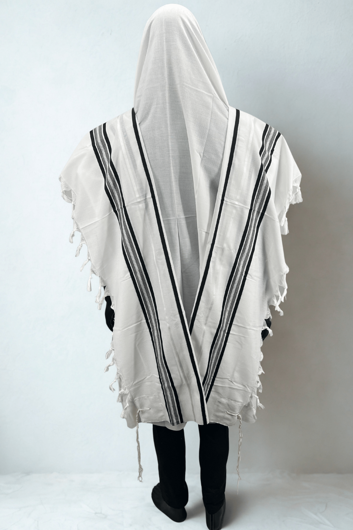 Person wearing a white prayer shawl with black stripes on a plain background