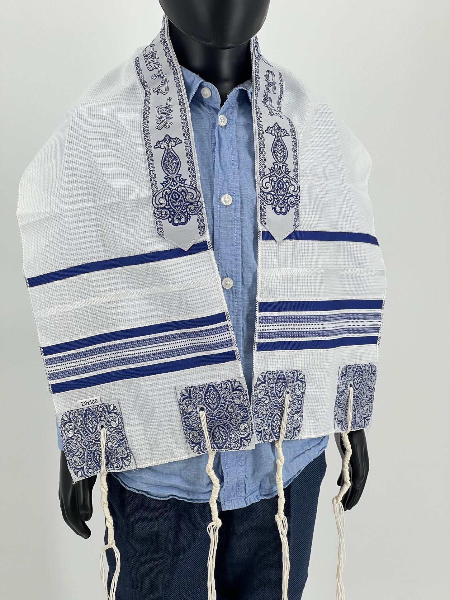 Child mannequin wearing a white children's tallit with dark blue stripes and decorative blue embroidered corners