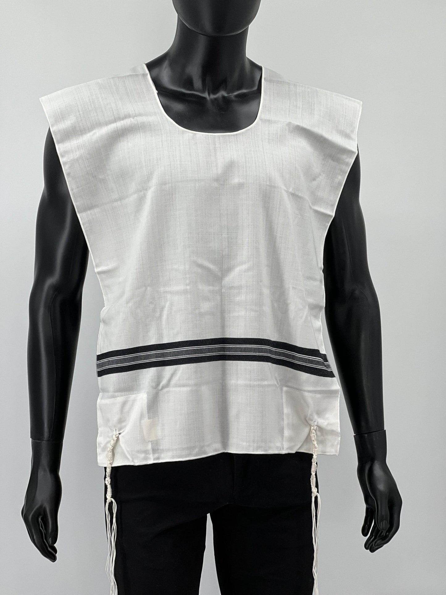 Front view of a mannequin wearing a white Tallit Katan with wide black striping across the chest and hand-tied Tzitzit strings hanging from the corners.
