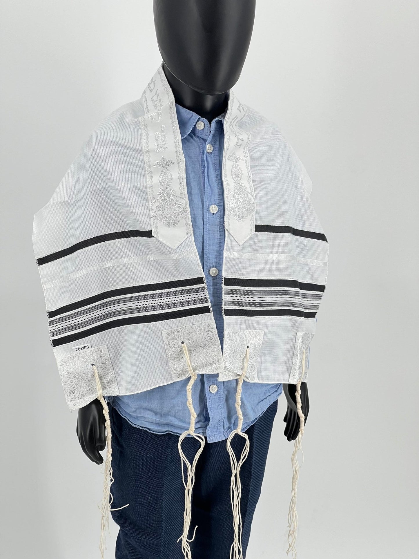 A children's tallit scarf displayed on a mannequin. The scarf is primarily white with black stripes and decorative elements.