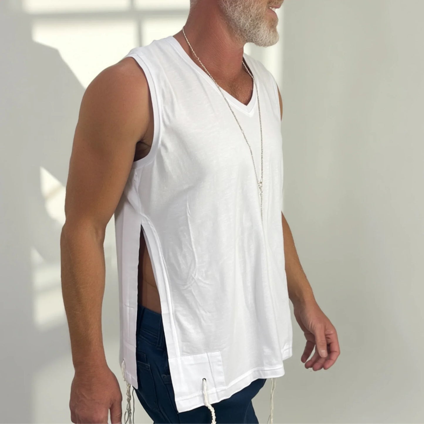 Man wearing a white Tzitzit sleeveless shirt, standing against a neutral background