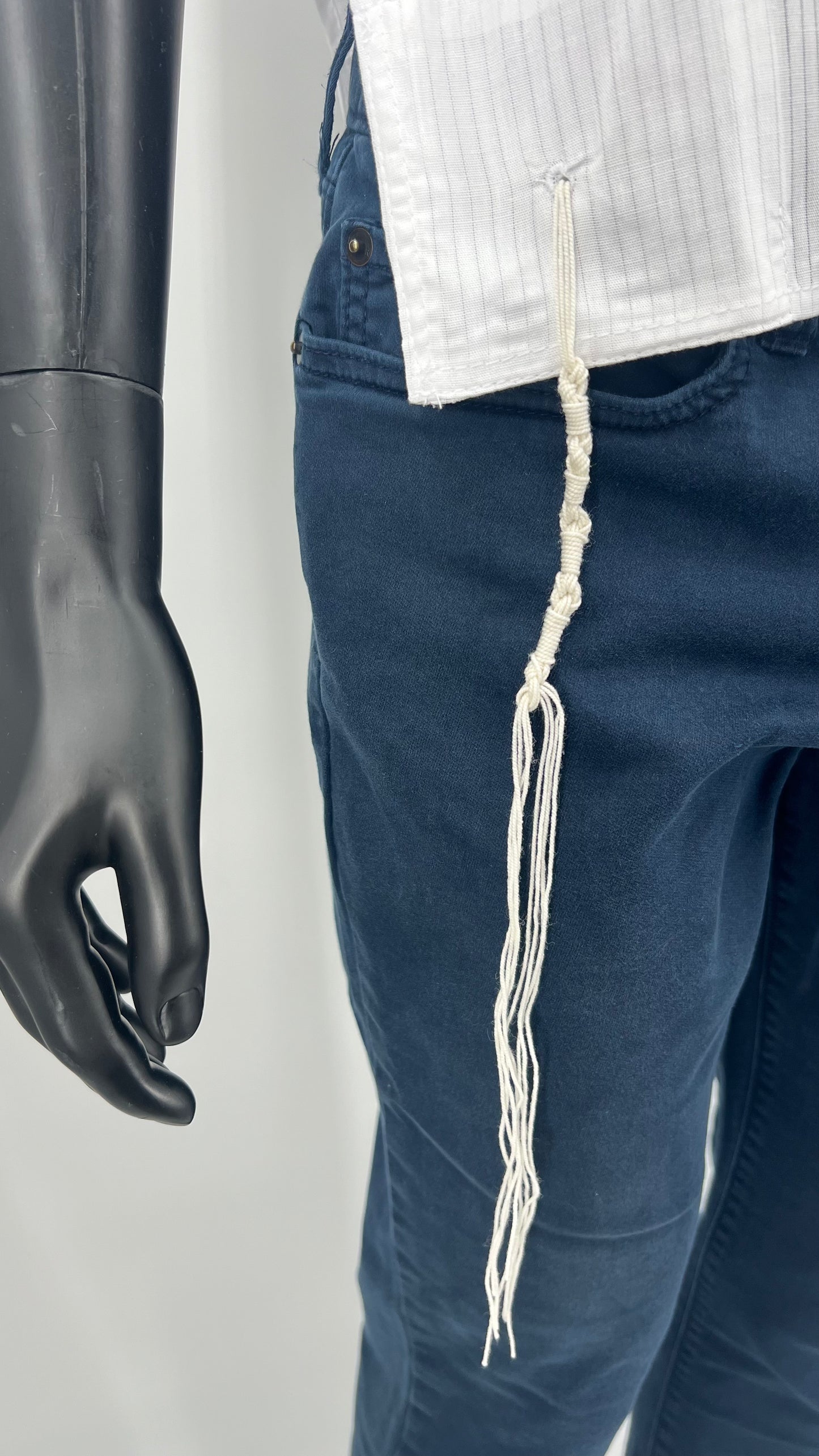 Close-up front view of Tzitzit on white cotton Tallit Katan worn on a black mannequin torso.