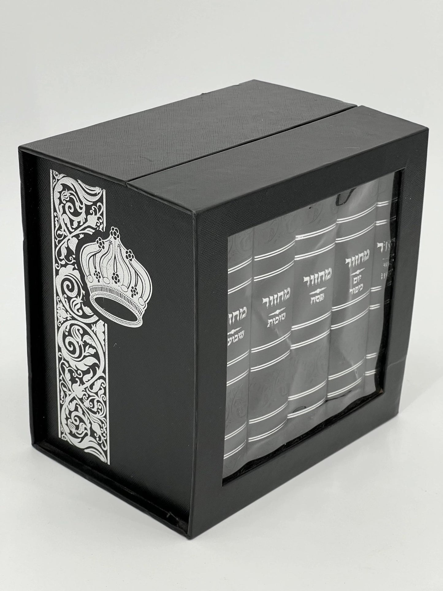 Five-volume Sha'arav B'Todah Sephardi Machzor set in a black faux leather case with a silver embossed crown and floral design. The front panel features a clear window displaying the white Hebrew titles of each machzor volume: Rosh Hashanah, Yom Kippur, Sukkot, Pesach, and Shavuot.