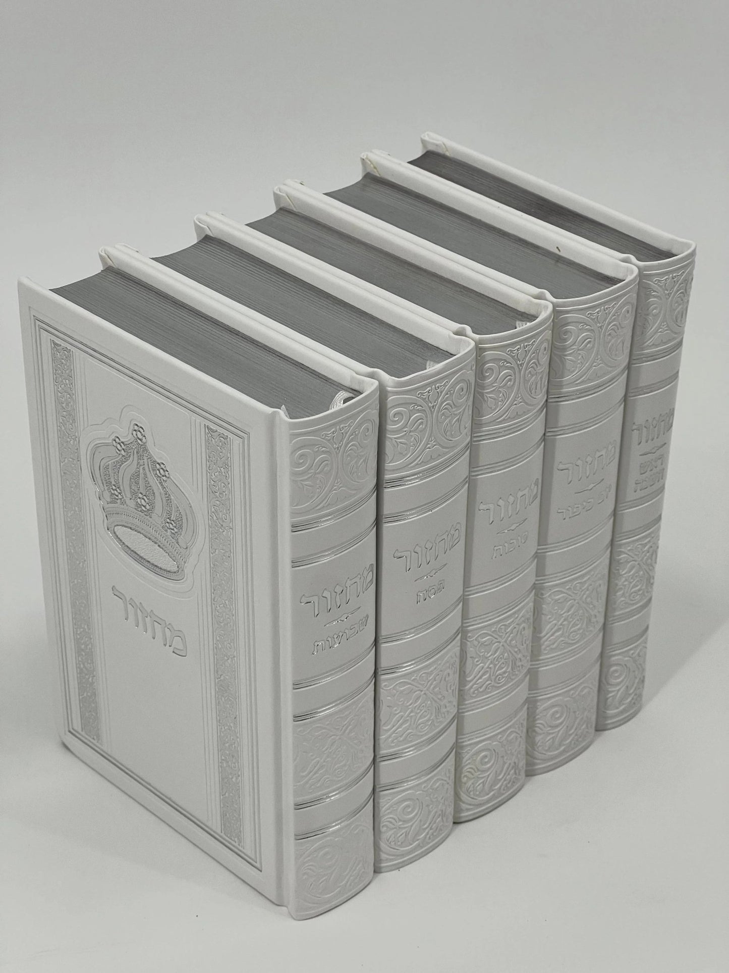 Five-volume Sha'arav B'Todah Sephardi Machzor set in elegant white faux leather with embossed Hebrew titles and crown design. Each volume corresponds to a major Jewish holiday: Rosh Hashanah, Yom Kippur, Sukkot, Pesach, and Shavuot. Decorative detailing enhances the spine and cover.