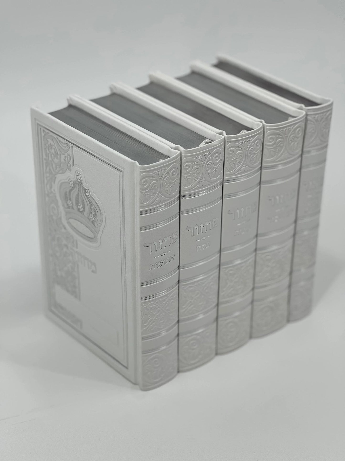 Five-volume Sha'arav B'Todah Sephardi Machzor set in elegant white faux leather with embossed Hebrew titles and crown design. Each volume corresponds to a major Jewish holiday: Rosh Hashanah, Yom Kippur, Sukkot, Pesach, and Shavuot. Decorative detailing enhances the spine and cover.