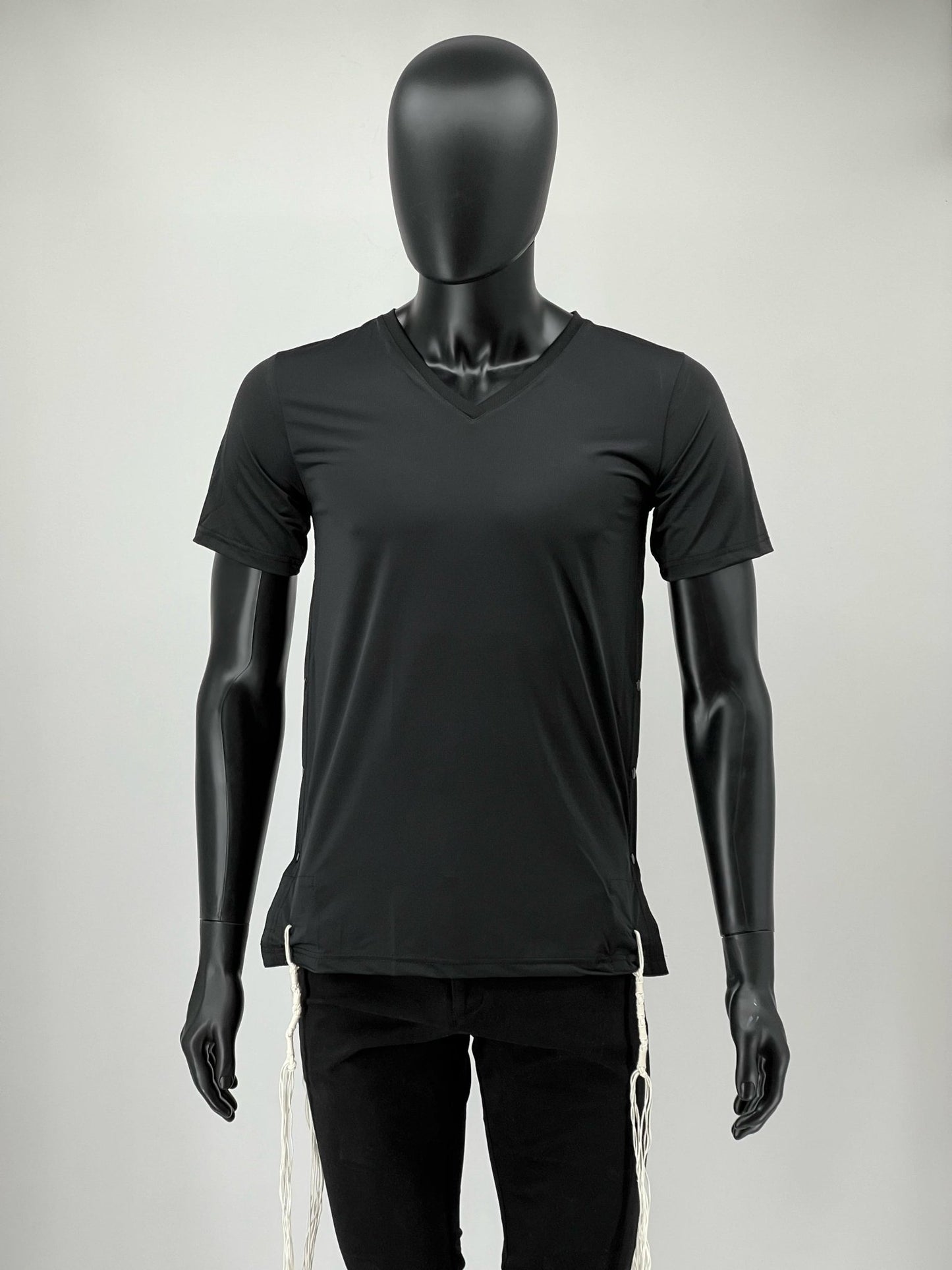 Front view of a mannequin wearing a black V-neck moisture-wicking Tzitzit T-shirt with white Tzitzit strings hanging from the corners. The shirt has a modern, athletic fit designed for everyday comfort.