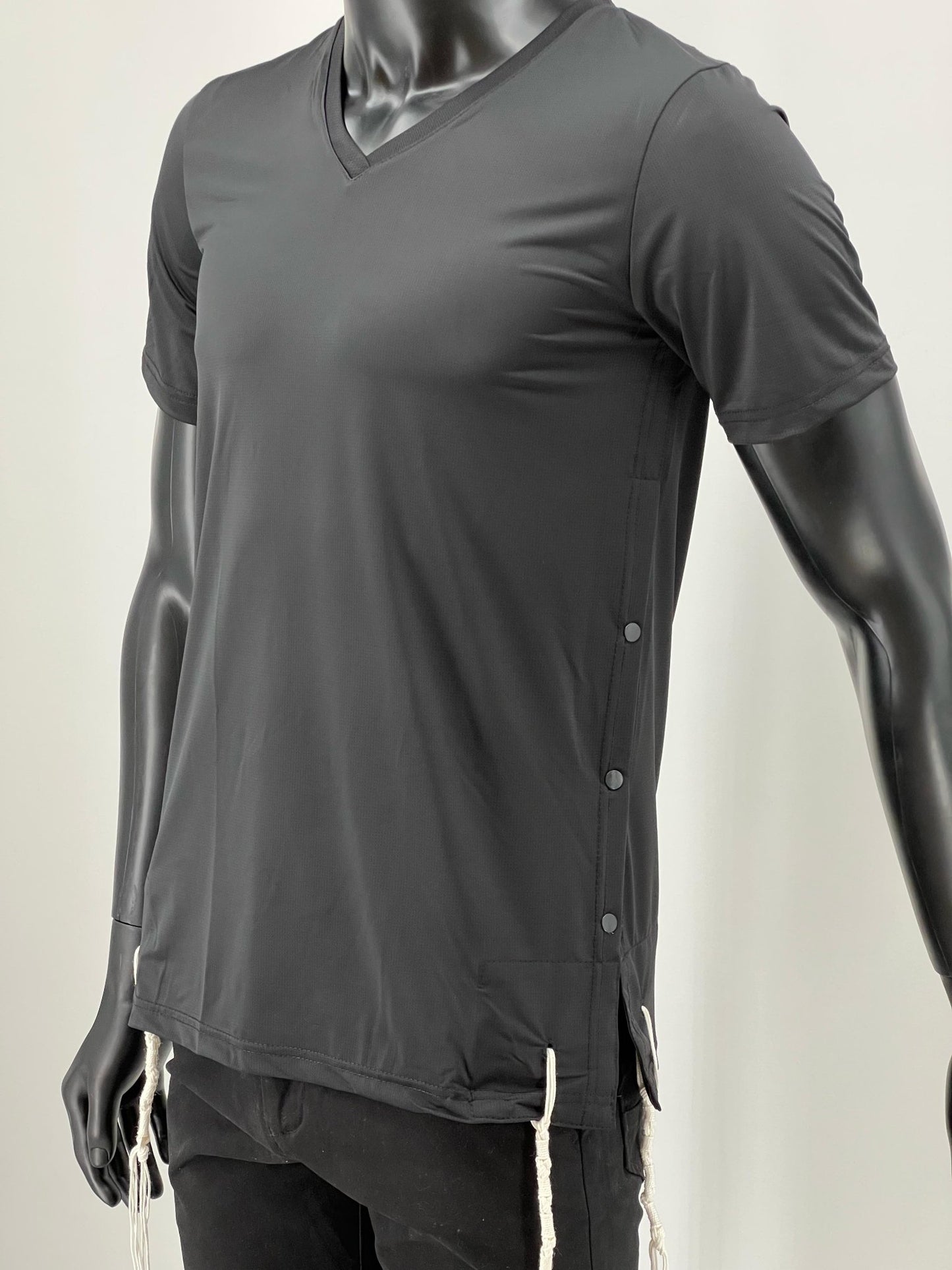 Black moisture-wicking V-neck Tzitzit T-shirt displayed on a mannequin. The shirt features a sleek athletic cut, discreet side buttons for ease of wear, and visible Tzitzit strings extending from the hem.