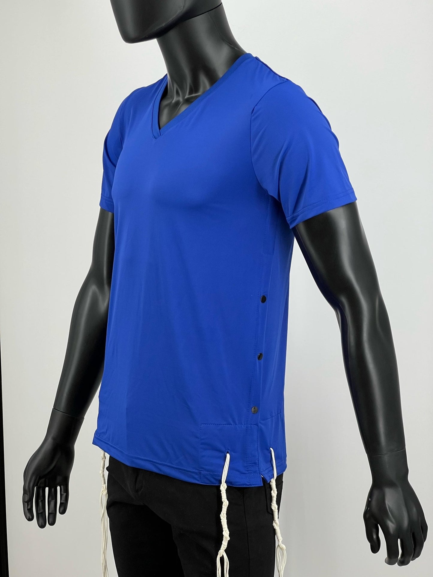 Side view of a mannequin wearing a royal blue V-neck moisture-wicking Tzitzit T-shirt with white Tzitzit strings attached at the corners. The shirt features side snaps for easy fastening and a modern athletic fit.