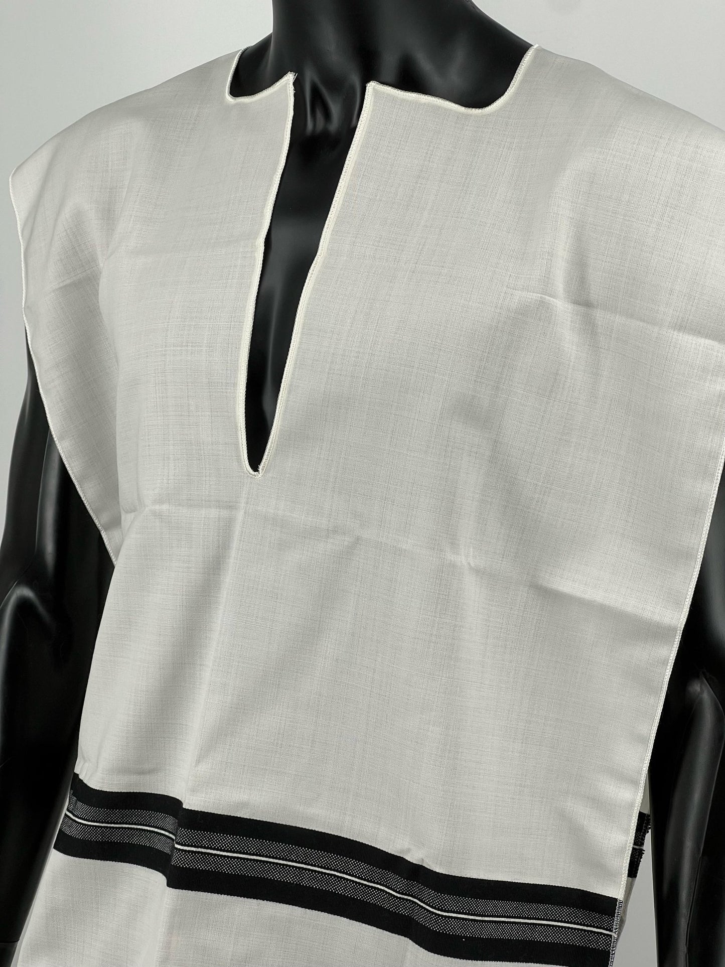 Close-up of a black mannequin wearing a white wool Tallit Katan with black striping and decorative fringe along the bottom.