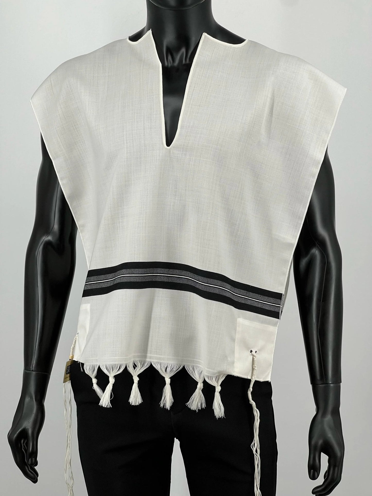 Front view of a black mannequin wearing a white wool Tallit Katan with black striping and decorative fringe along the bottom.