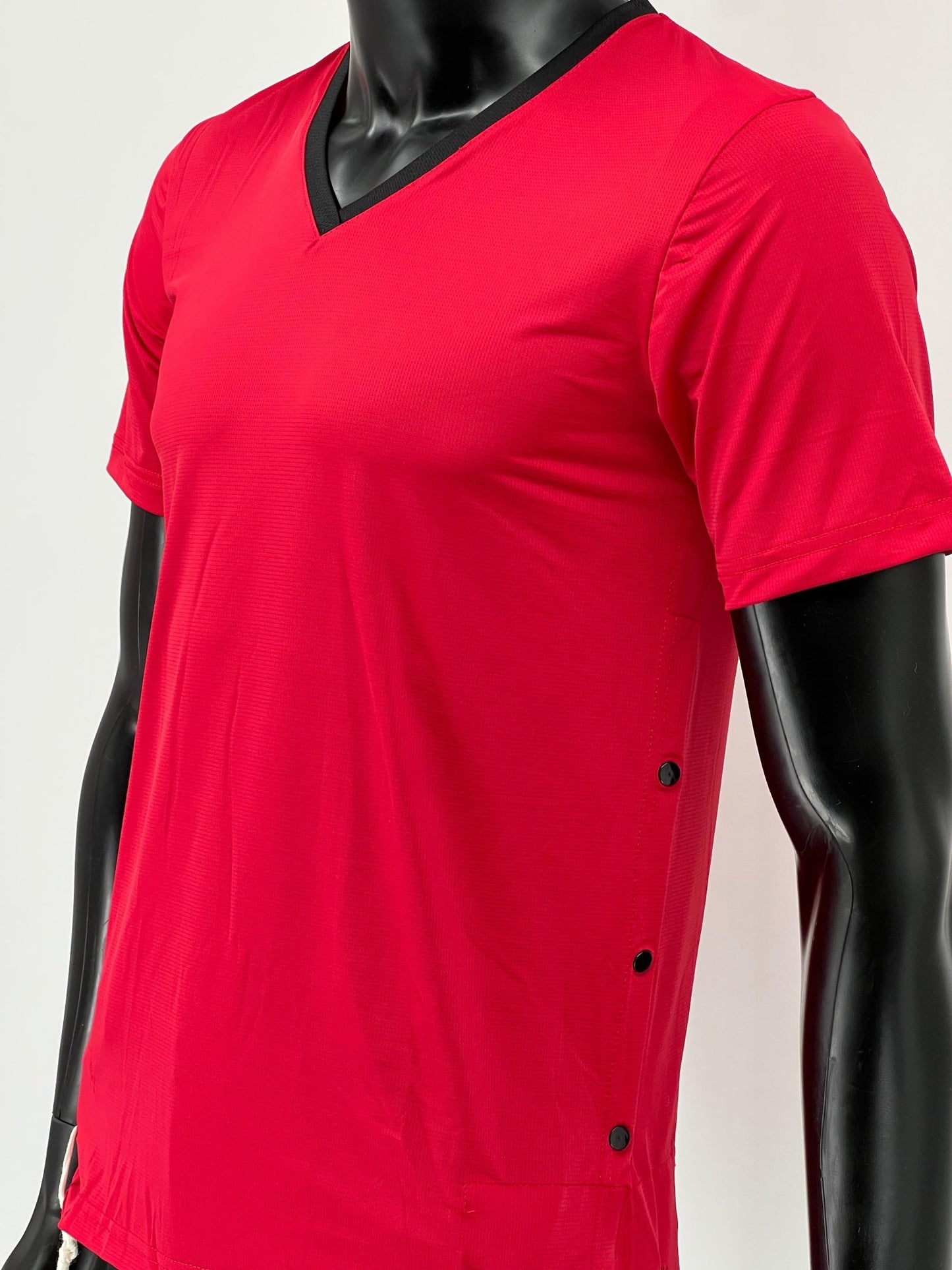 Side view of a red athletic Tzitzit T-shirt featuring a black V-neck collar and side snap buttons. The shirt is worn by a mannequin and includes attached white Tzitzit strings at the hem.