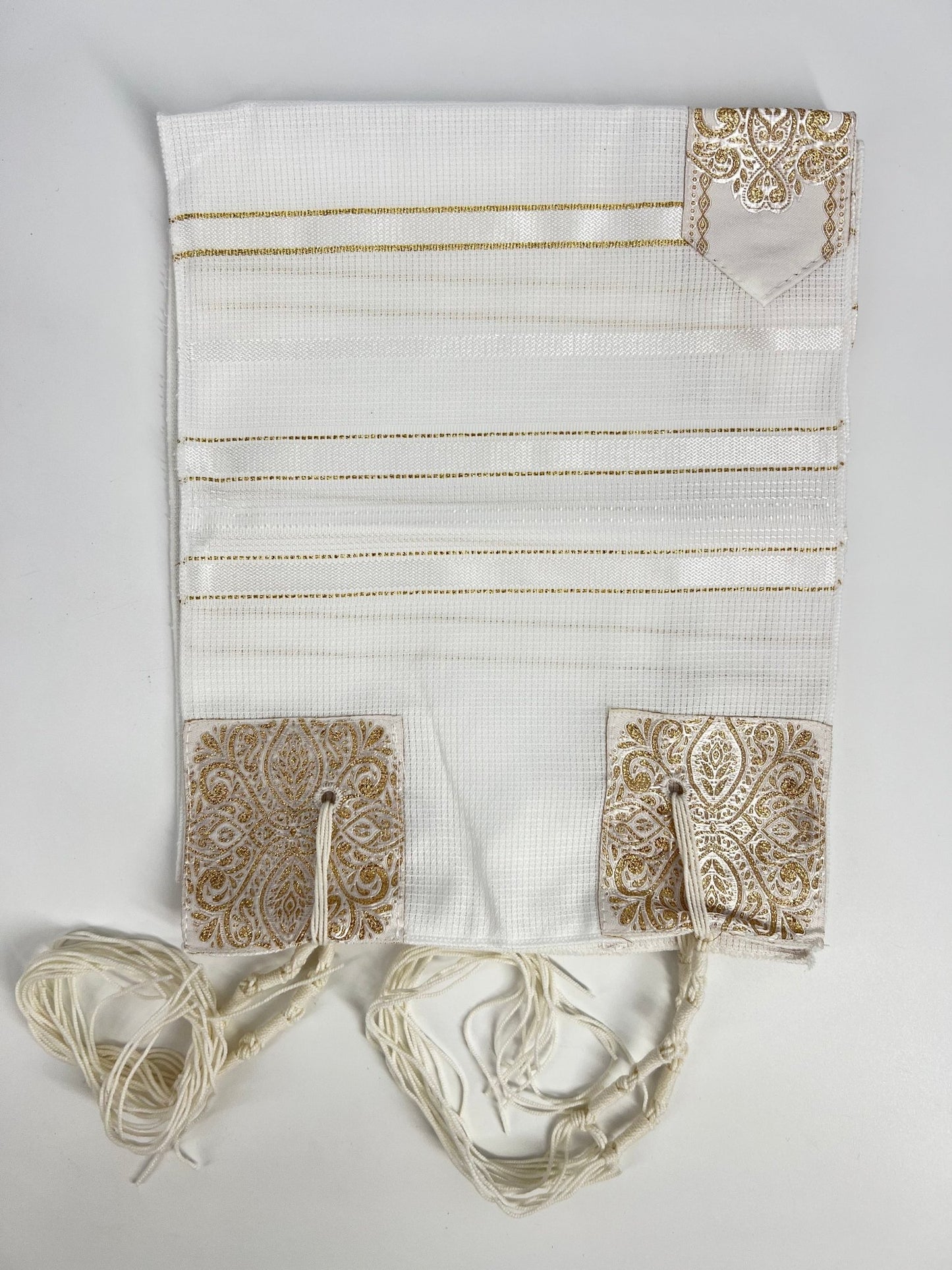 Folded white children's tallit (Jewish prayer shawl) featuring gold stripes, decorative gold corner reinforcements