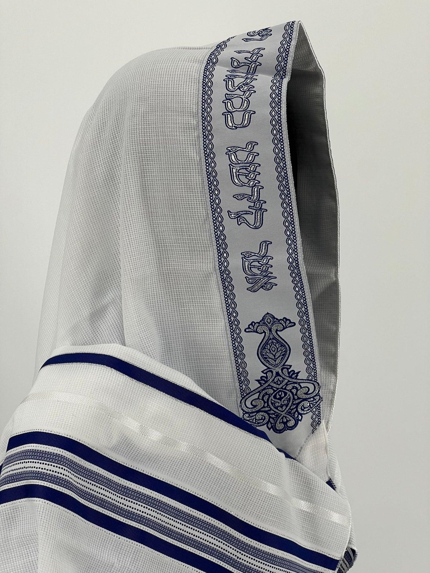 Close-up side view of a white children's tallit (Jewish prayer shawl) with dark blue stripes and a decorative atara