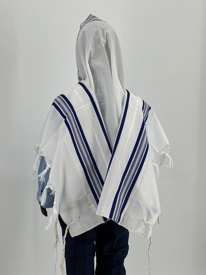 The tallit features traditional tzitzit (fringes) at the corners and is worn over a light blue shirt and dark pants.