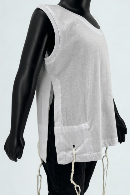 Close-up side view of a child mannequin wearing a sleeveless white Tzitzit T-shirt with halachically tied fringes (Tzitzit) on the corners. The shirt features wide side openings and reinforced stitching, shown paired with black pants, against a light background.