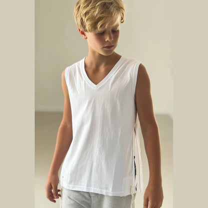 Young boy wearing a white Tzitzit T-shirt sleeveless and gray pants against a plain background
