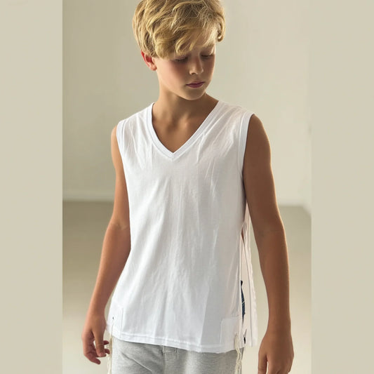 Young boy wearing a white Tzitzit T-shirt sleeveless and gray pants against a plain background