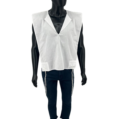 A full-body view of a black mannequin wearing a white cotton Tallit Katan with subtle vertical stripes. The garment has a V-neck opening and features long kosher tzitzit strings hanging from all four corners. The mannequin is dressed in dark pants, and the tallit katan is worn over them.