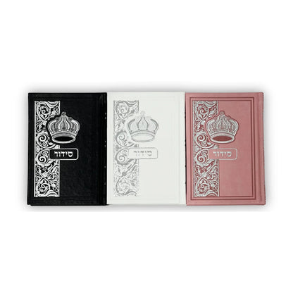 Set of three faux leather Siddurim (prayer books) in black, white, and pink. Each book features an embossed silver crown and floral pattern with the Hebrew word "סידור" on the cover. The books are arranged upright side by side