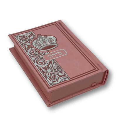 Pink aux leather Siddur with an embossed crown and decorative floral design on the cover. The Hebrew word "סידור" appears in silver foil in the center. The book is slightly angled and closed, showing its elegant edges and craftsmanship.