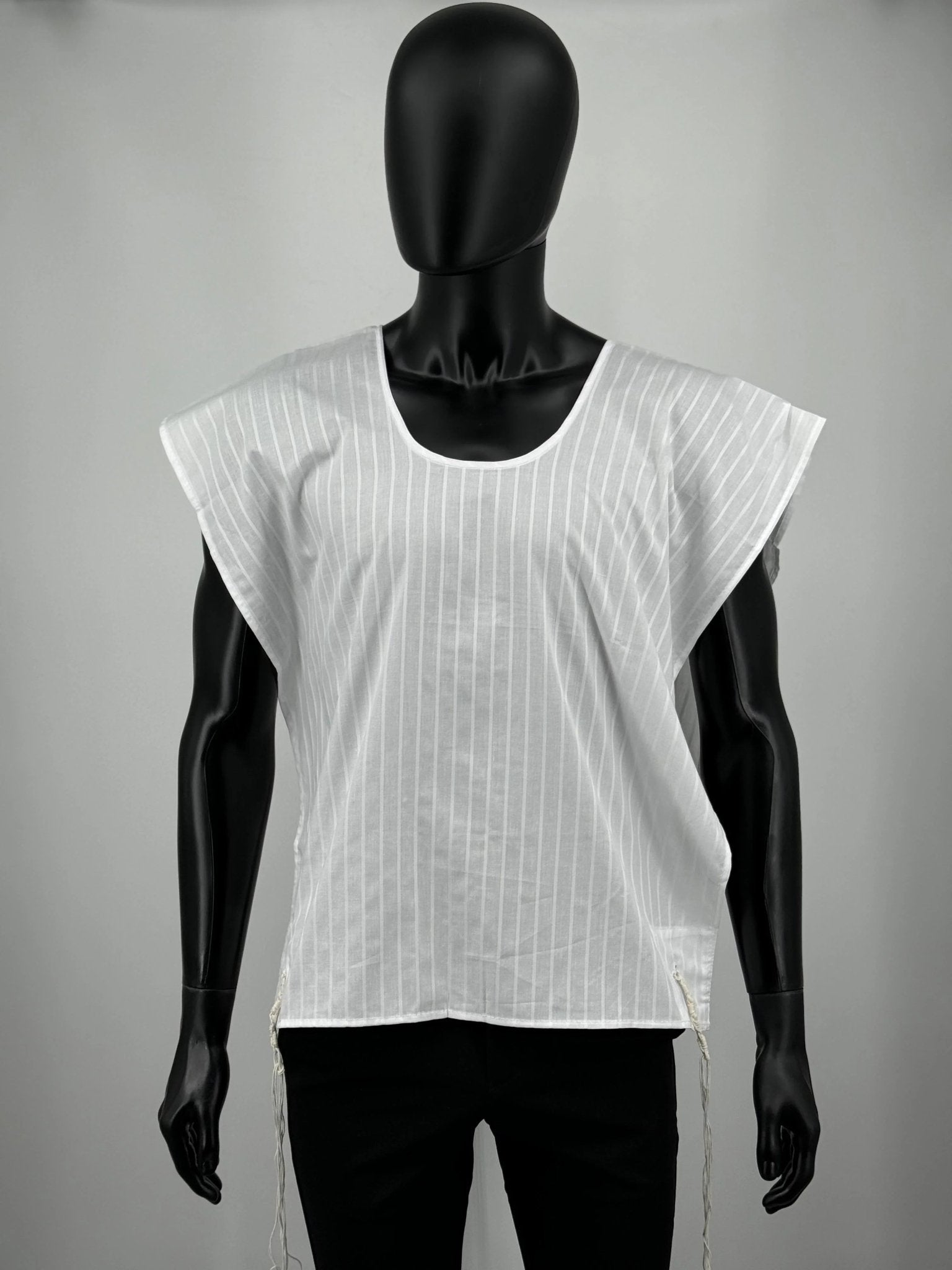 A white cotton Tallit Katan with vertical textured stripes, shown on a black mannequin torso. The garment features a V-shaped neckline and tzitzit strings hanging from the two front corners.