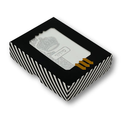 White  faux leather Siddur with silver embossed crown design, displayed in a black-and-white striped gift box with a clear window. Hebrew word "סידור" appears on the cover. The box features a gold "MMJ" logo at the bottom.