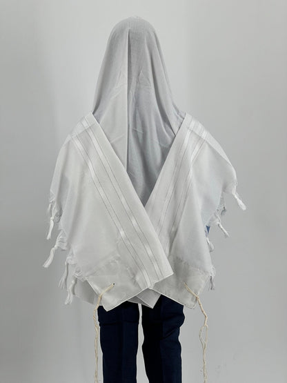 Child wearing a white tallit (Jewish prayer shawl) with subtle white-on-white striping, viewed from the back.