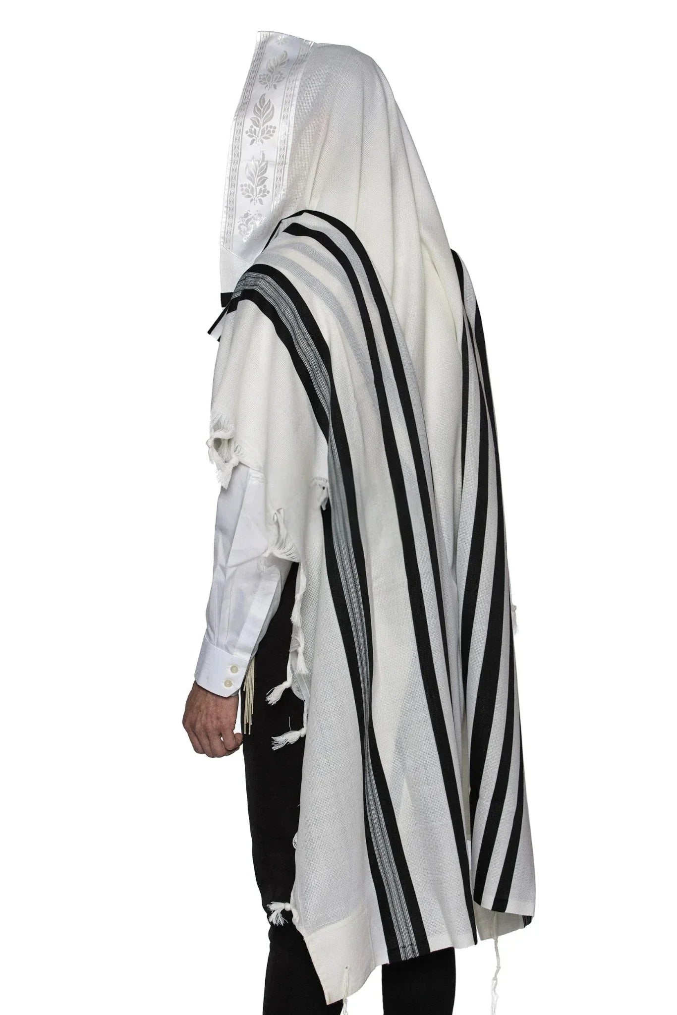 Man wearing a white wool Tallit with black stripes. Tallit features knotted tzitzit and decorative fringe along the edges.