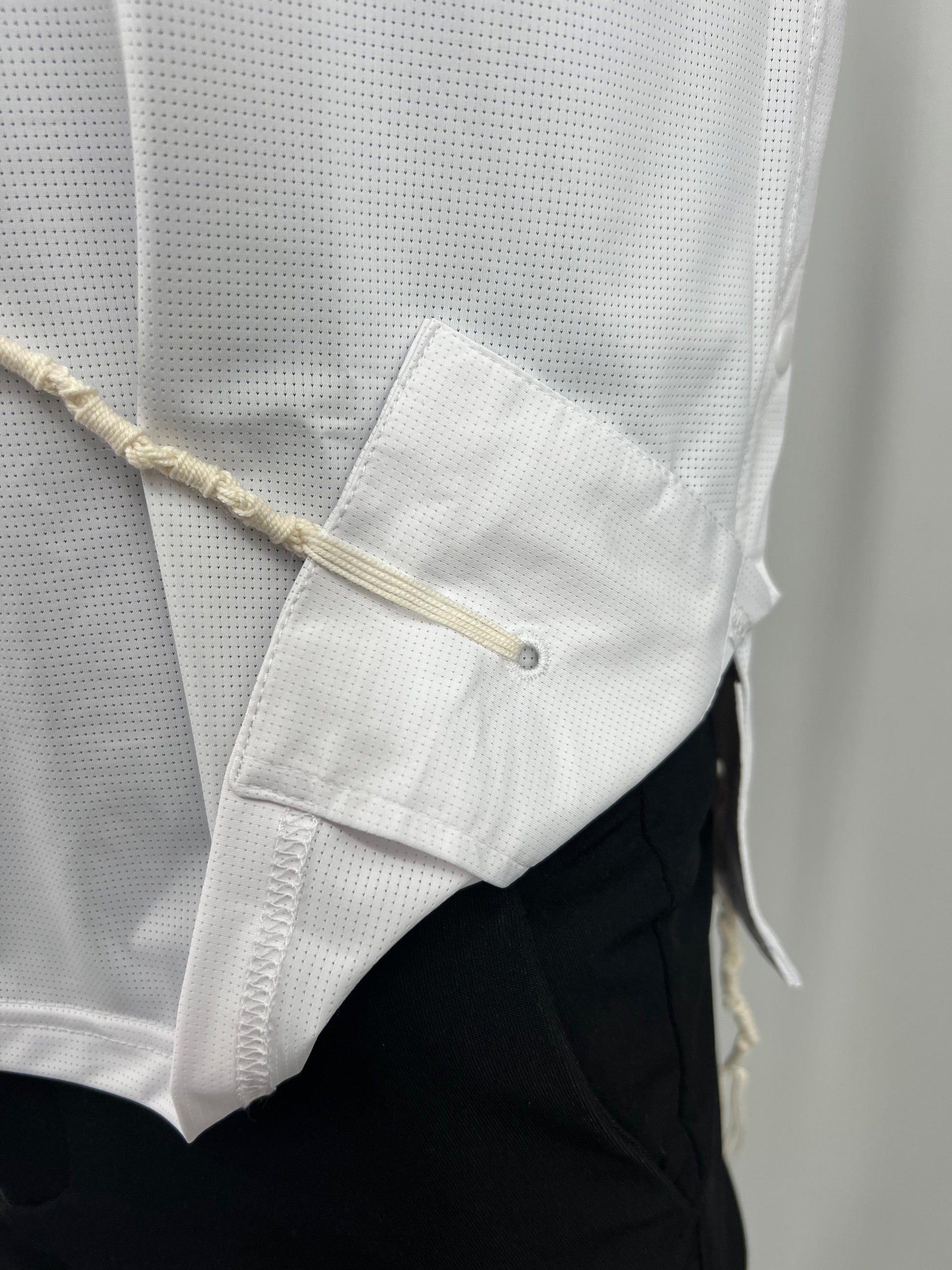 Close-up of a white shirt with a tzitzit pocket and black pants against a neutral background
