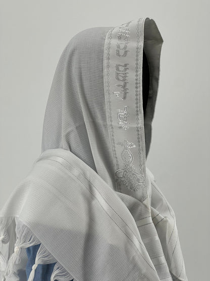 Child mannequin wearing a Jewish prayer shawl with an embroidered silver Hebrew blessing along the edge of the hood.