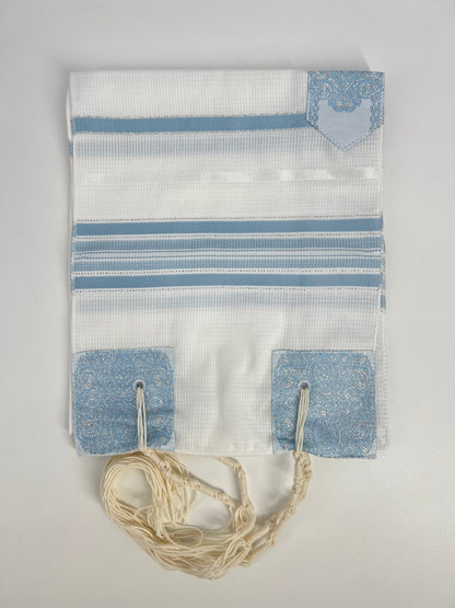 Folded white children's tallit (Jewish prayer shawl) featuring light blue stripes, decorative silver corner reinforcements