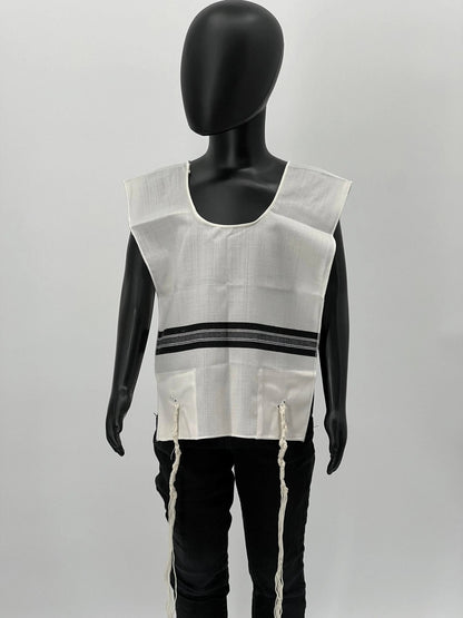 Child-sized mannequin wearing a white wool Chabad Tallit Katan with black striping and a rounded neckline. The garment includes kosher tzitzit strings hanging from all four corners and is designed according to traditional Jewish standards.