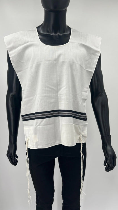 Child-sized mannequin wearing a white wool Tallit Katan with black striping and a rounded neckline. The garment includes kosher tzitzit strings hanging from all four corners and is designed according to traditional Jewish standards.