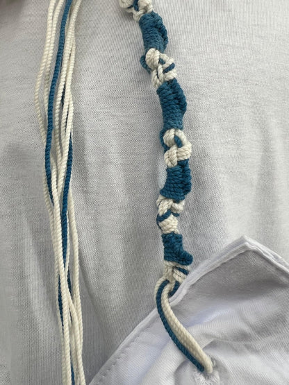 Close-up of a white Tzitzit T-shirt with a reinforced corner pocket showing tied Tzitzit strings,