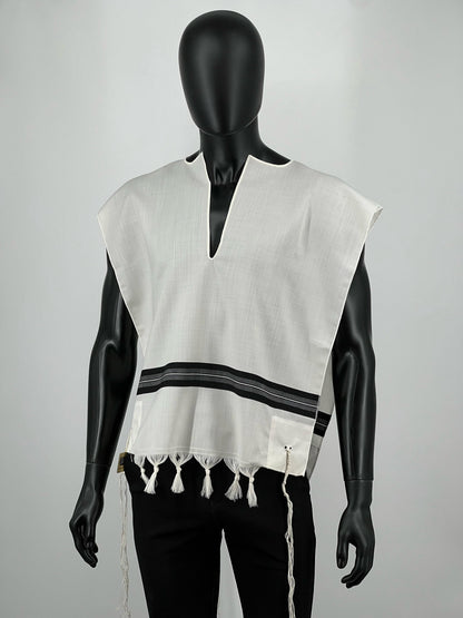Front view of a black mannequin wearing a white wool Ashkenazi Tallit Katan with black striping and decorative fringe along the bottom. The garment features a halachic V-neck opening and long, knotted kosher tzitzit strings hanging from all four corners.